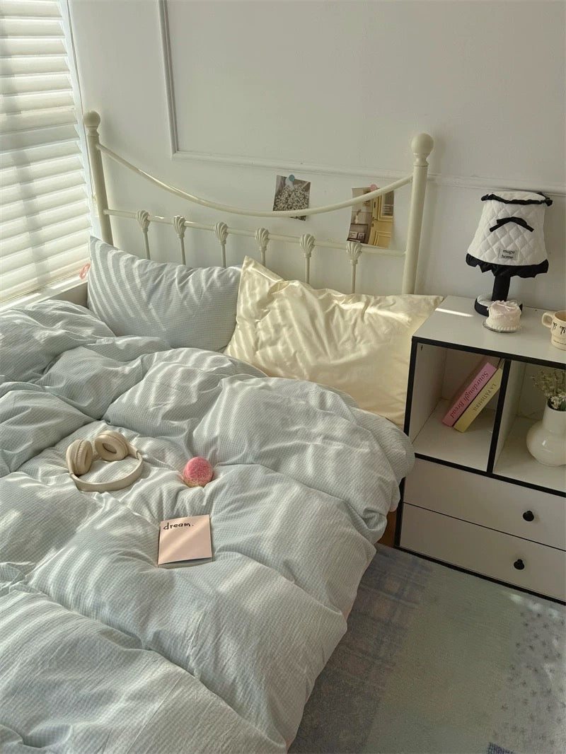 Bedroom with light blue bedding, pillows, and a nightstand with a lamp.