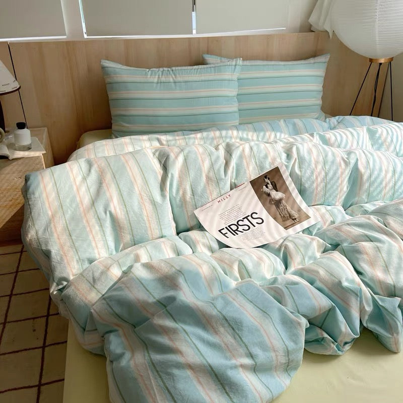 Bed with striped bedding and pillows in a room with a lamp and window.