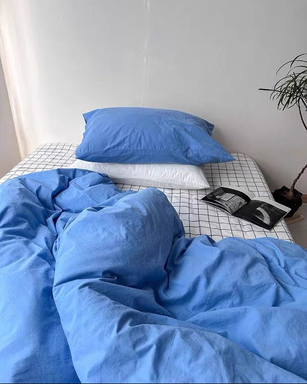Bed with blue bedding and pillows against a white wall.