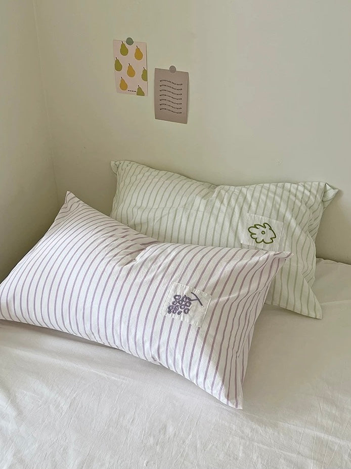 Lavender striped pillowcase with small grape embroidery in front of a sage striped flower pillowcase.