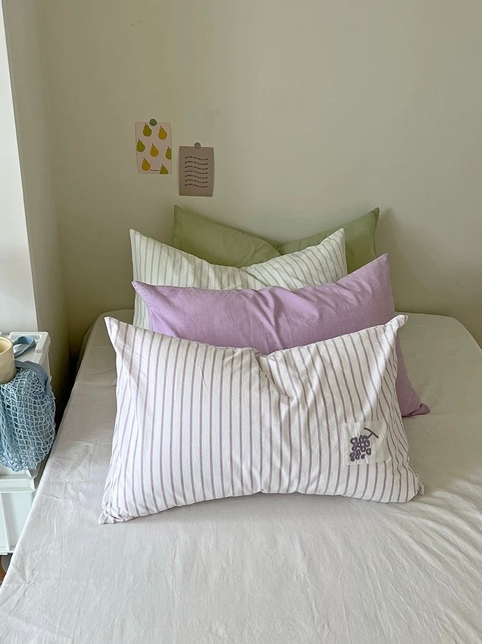 Lavender grape embroidered pillowcase resting in front of sage green and lilac pillows on a made bed.