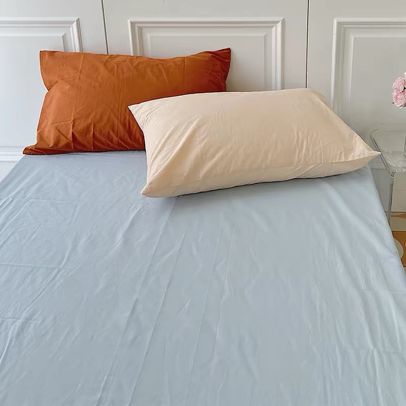 An orange pillow and a cream pillow sit above a light blue sheet in a close view of the bed.