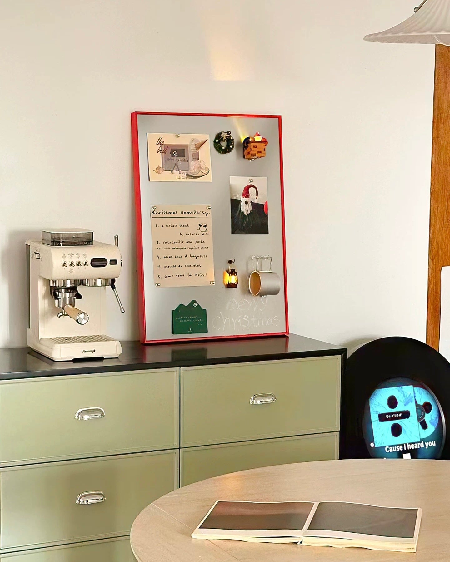 A red-framed magnetic cork board with various notes, photos, and small accessories displayed on a dark cabinet in a styled home office setting.