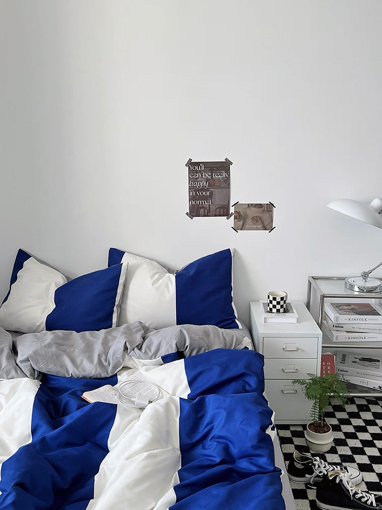 Bedroom with blue and gray bedding, nightstand, and decorative items on a white wall.