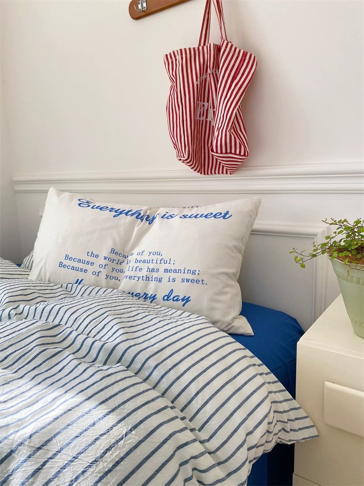 Bed with striped bedding and pillow, red and white bag on headboard, plant on nightstand