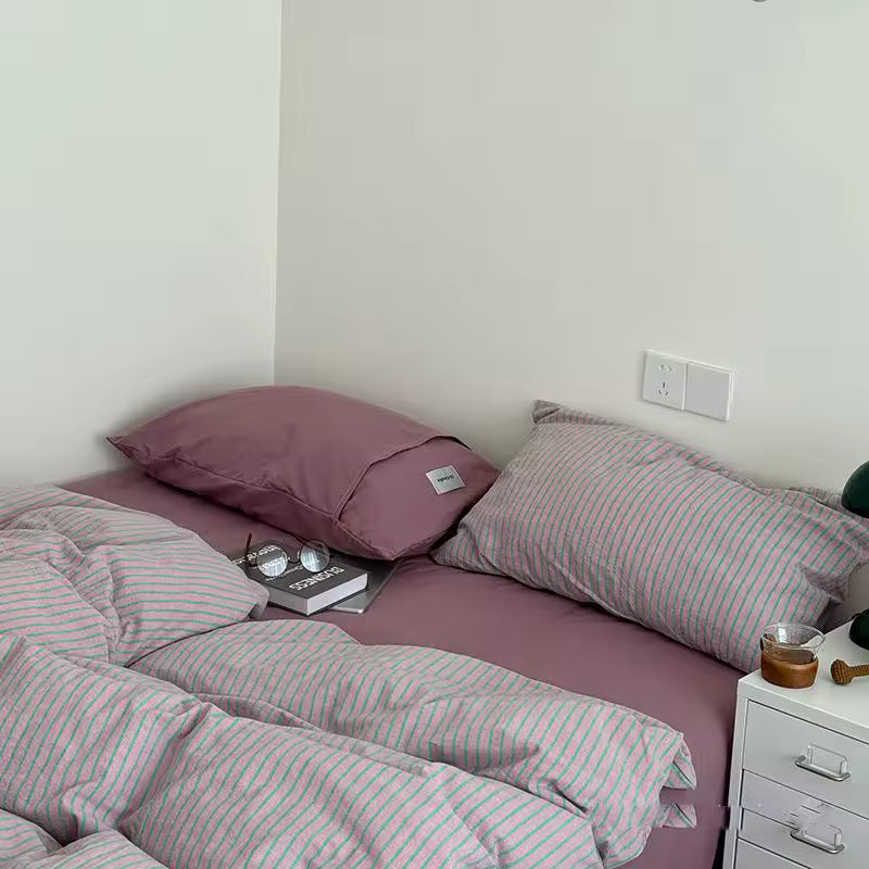 Bed with striped bedding and pink pillows in a room setting.