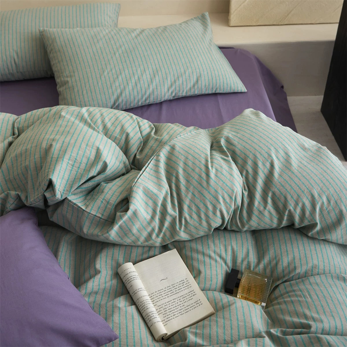 Bed with green and white striped bedding and a book on a purple pillow