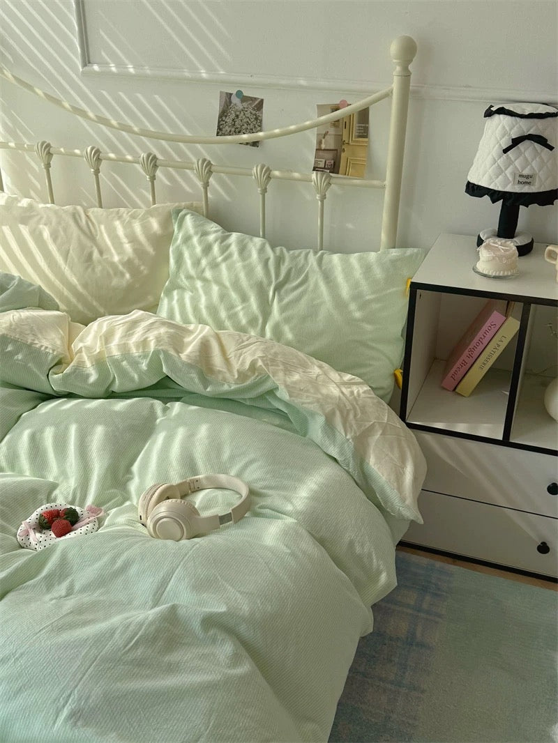 Bedroom with light green bedding and a nightstand with a lamp.