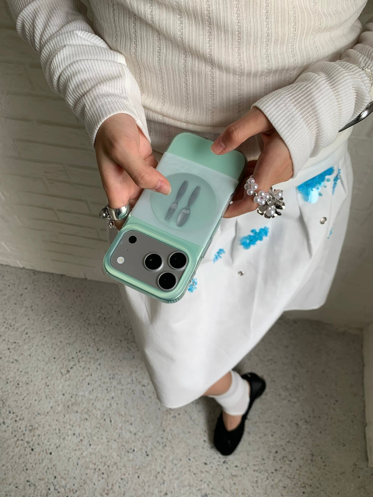 A mint green iPhone case viewed from above in one hand, with the tableware design facing outward.