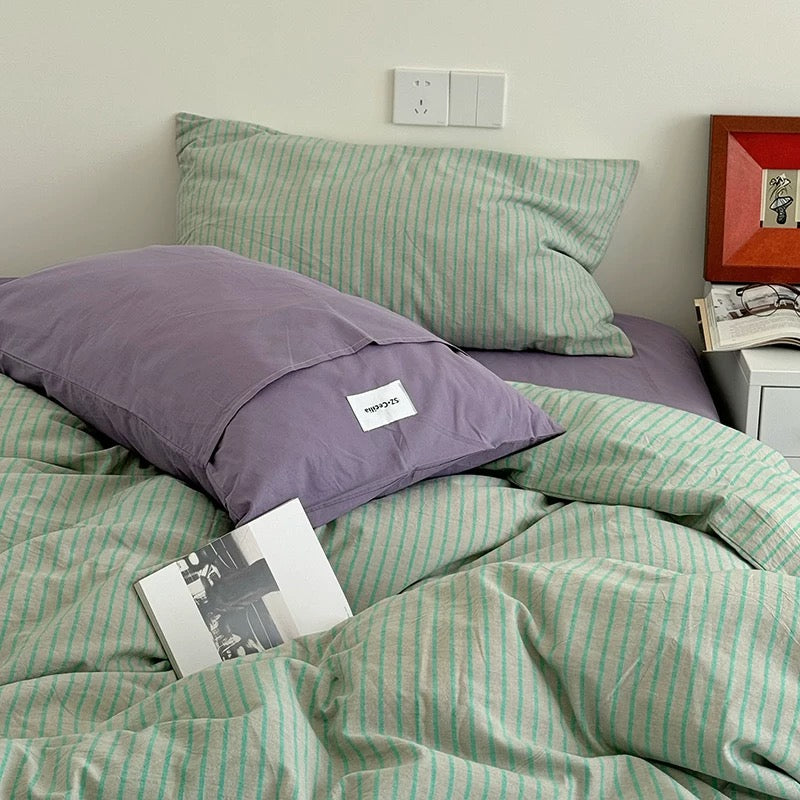 Bed with green and purple striped bedding and pillows, with a book on the bed.