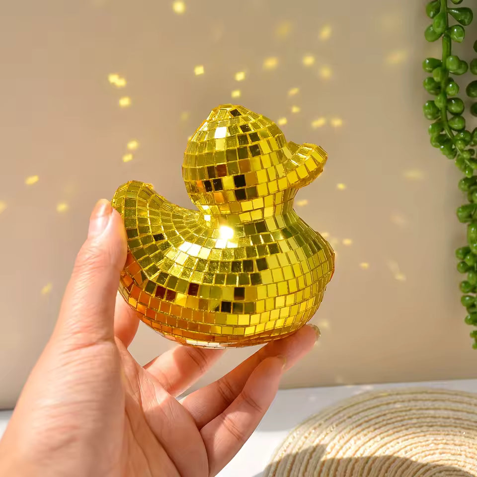 Hand holding a disco ball rubber duck against a neutral background