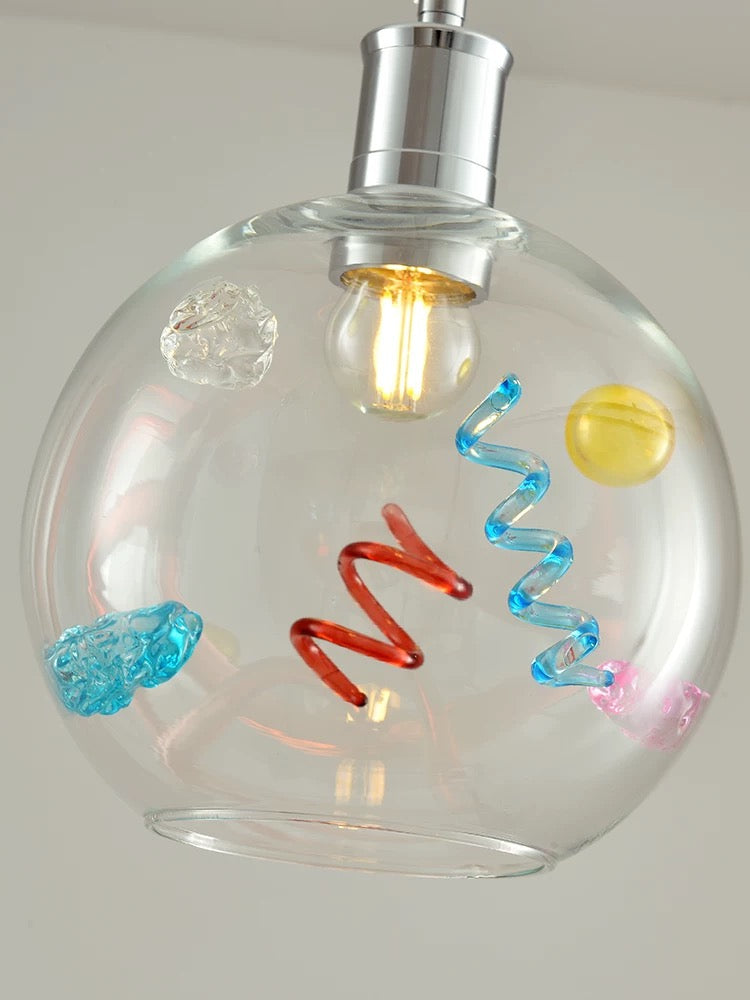 Clear glass pendant light with colorful decorations on a neutral background