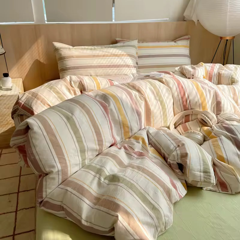 Striped bedding on a bed in a room with a lamp and window.