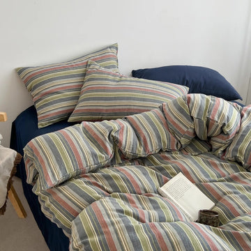 A bed dressed in a striped duvet cover and matching pillowcases with blue pillows, styled in a bedroom setting with a book on the duvet.