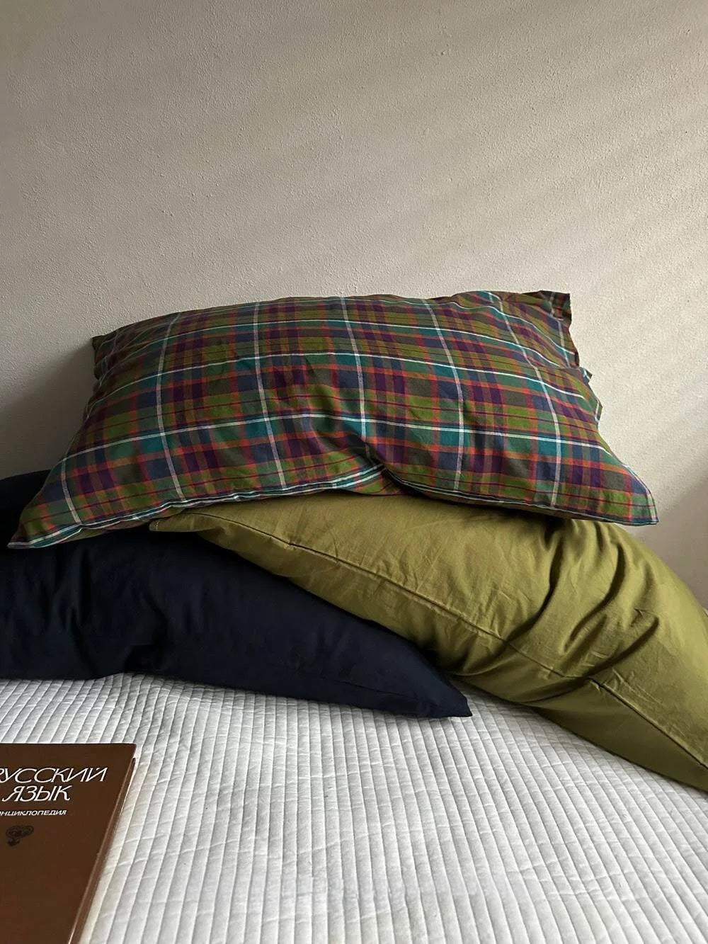 Multicolor plaid pillowcases layered over olive green and navy on a white bed.