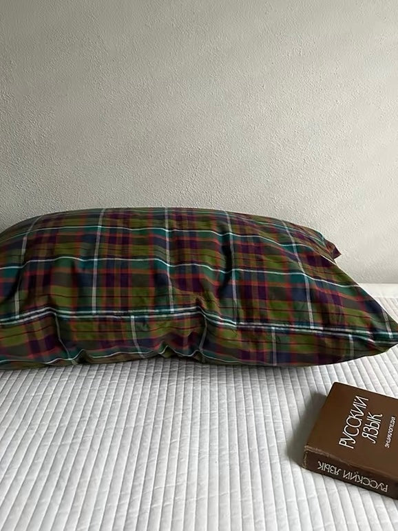 A single pillowcase with multicolor plaid against a cream wall on white bedding.