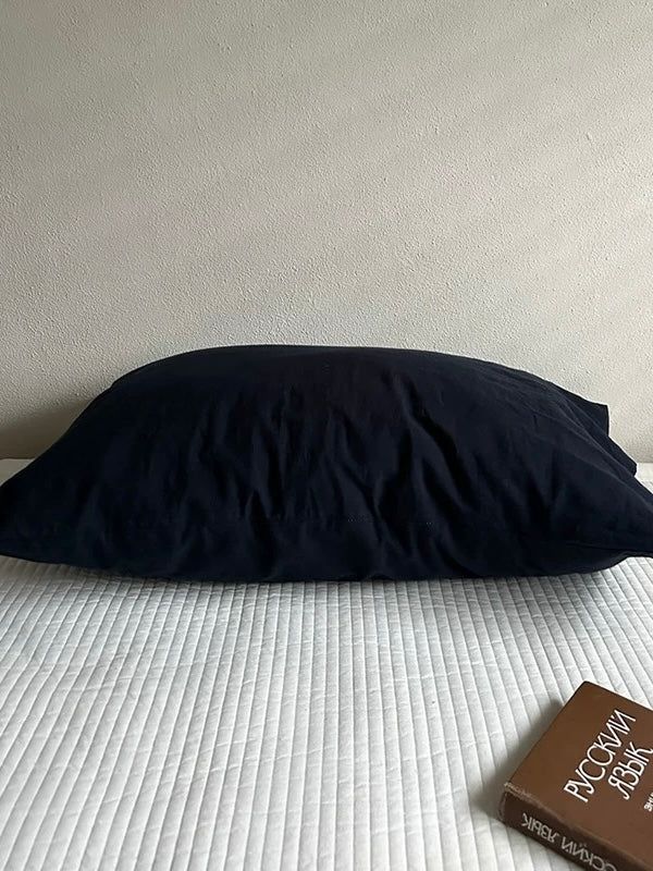 A navy blue pillowcase resting alone on white bedding.