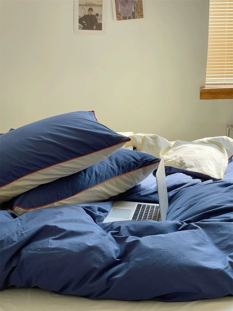 Bed with blue bedding and pillows, laptop open on a surface, light-colored wall with framed pictures.