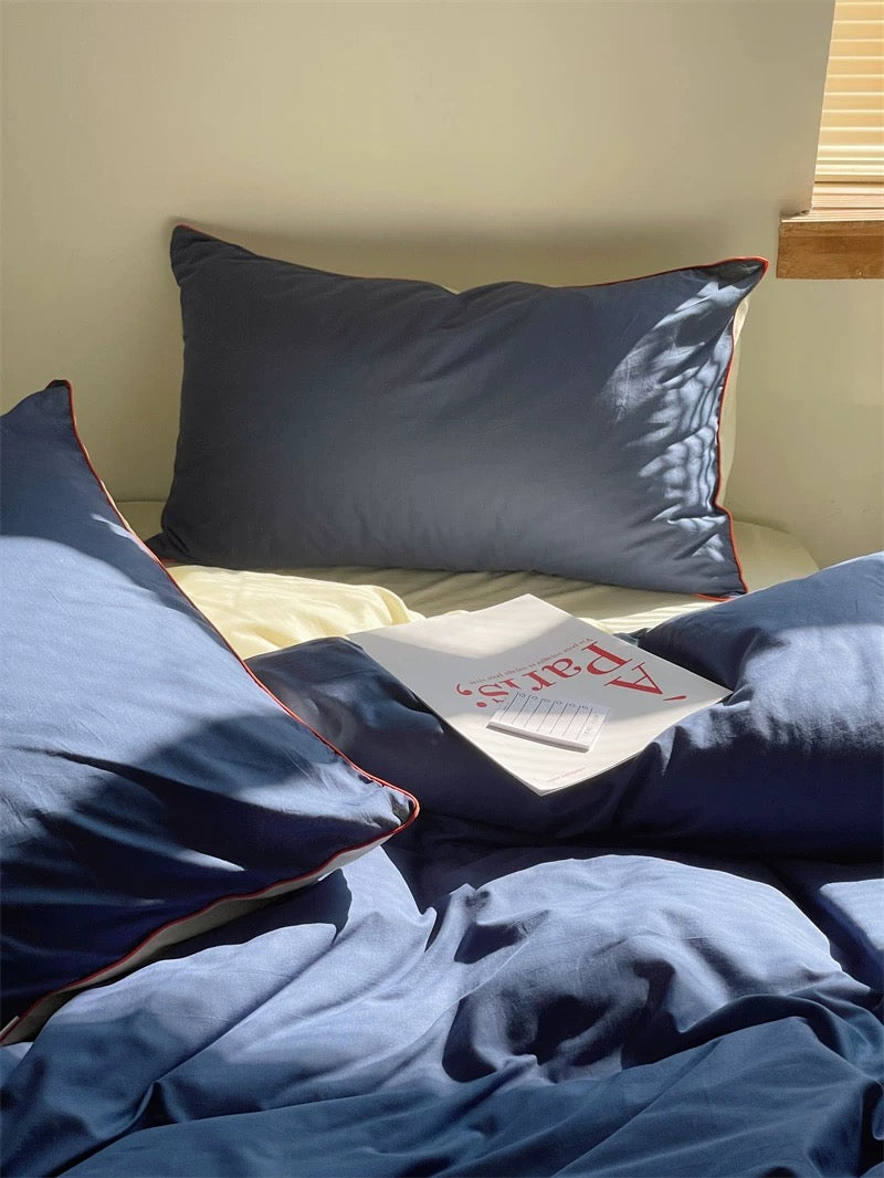 Blue satin pillows on a bed with a magazine underneath.