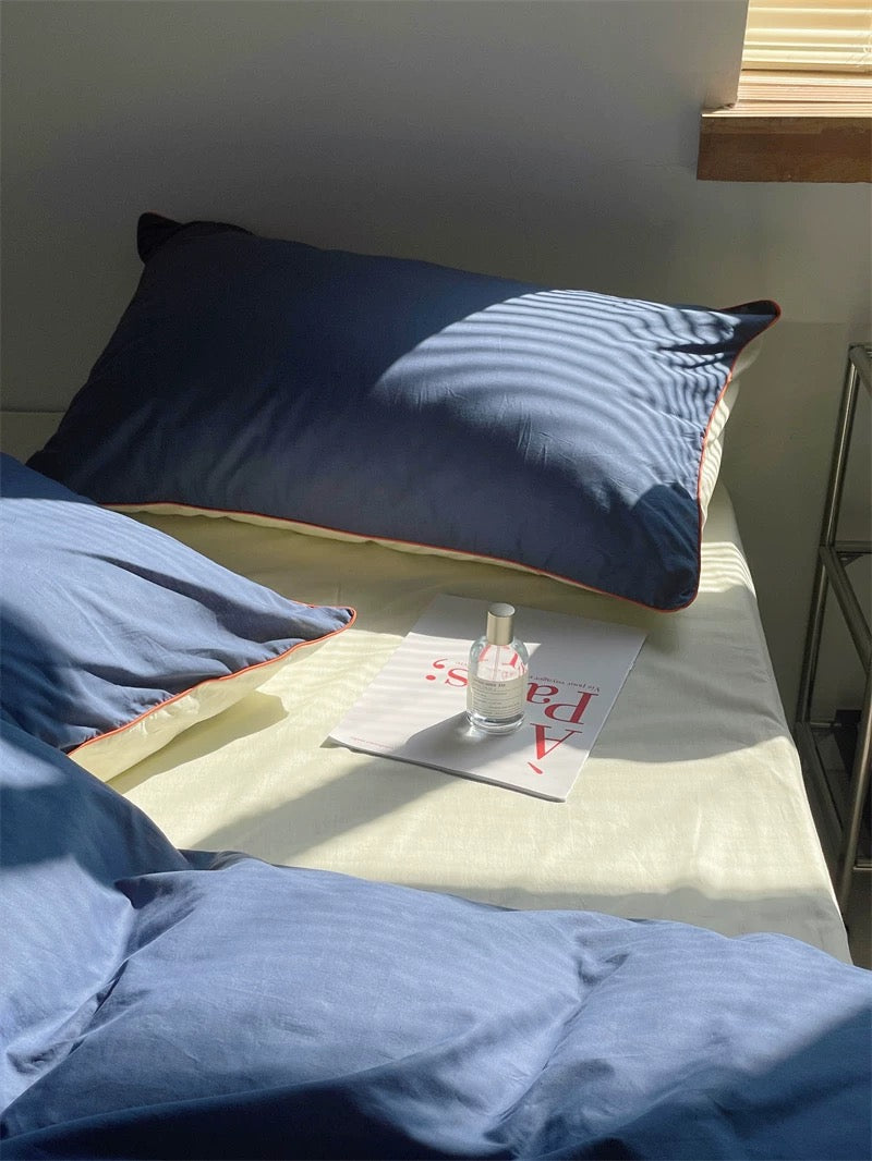 Blue pillows on a bed with a magazine and bottle of nail polish on a nightstand.