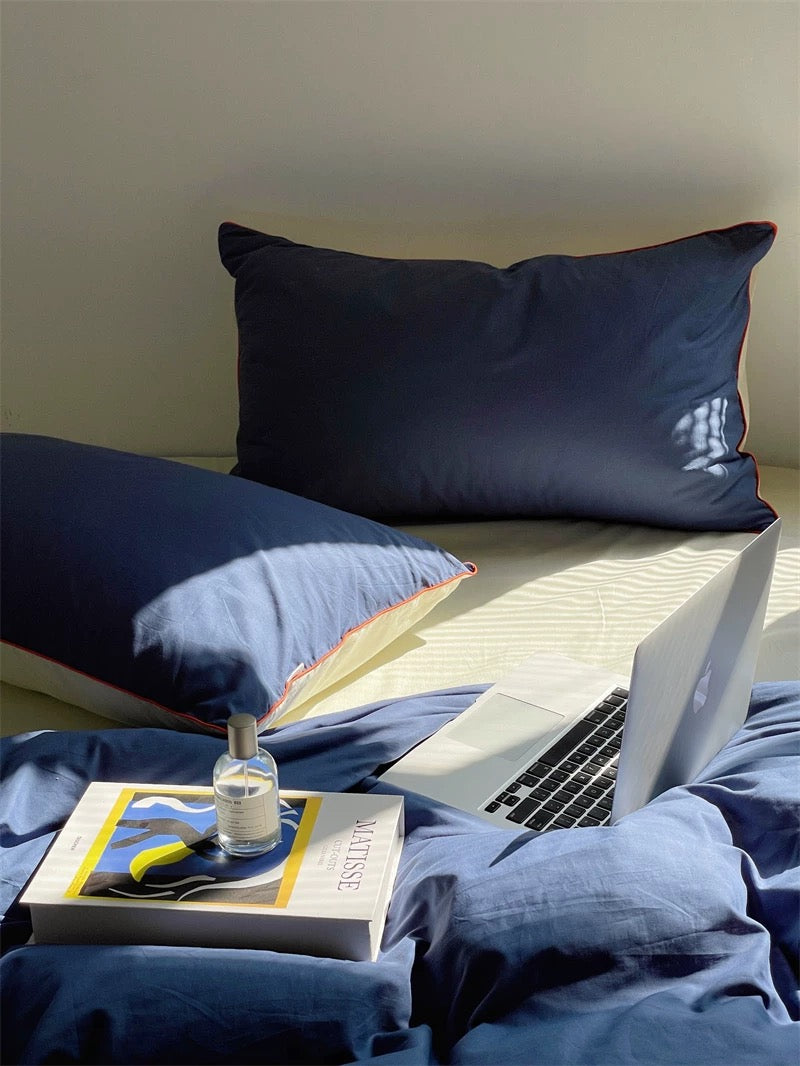 Navy blue pillows and bedding with a laptop and book on a bed.
