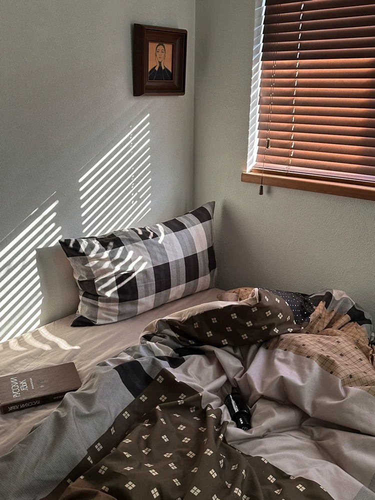 Neutral plaid bedding arranged below a window with wooden blinds