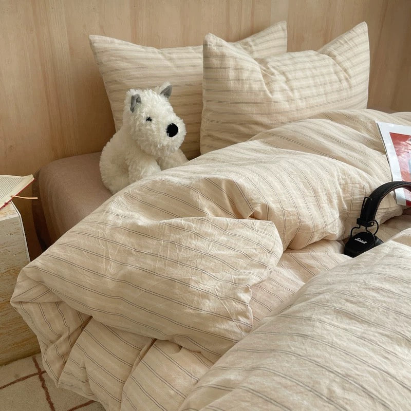 Beige striped bedding on a bed with a plush toy and magazine.