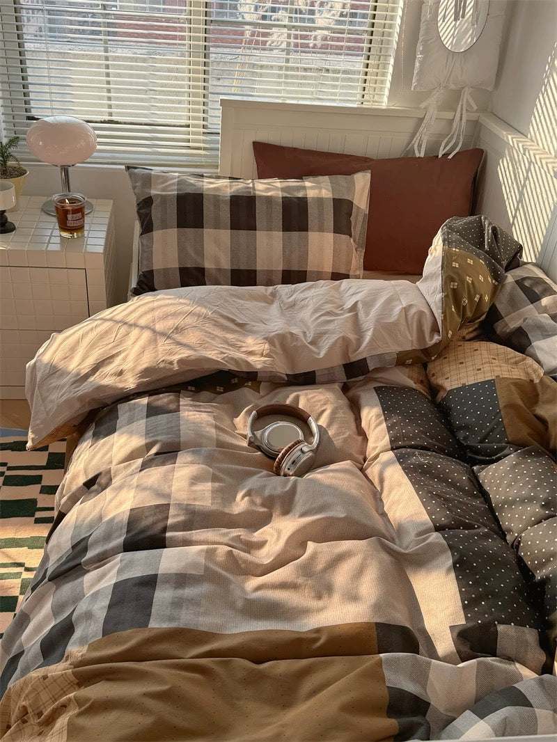 Bed with checkered bedding and pillows in a room with a window and nightstand.