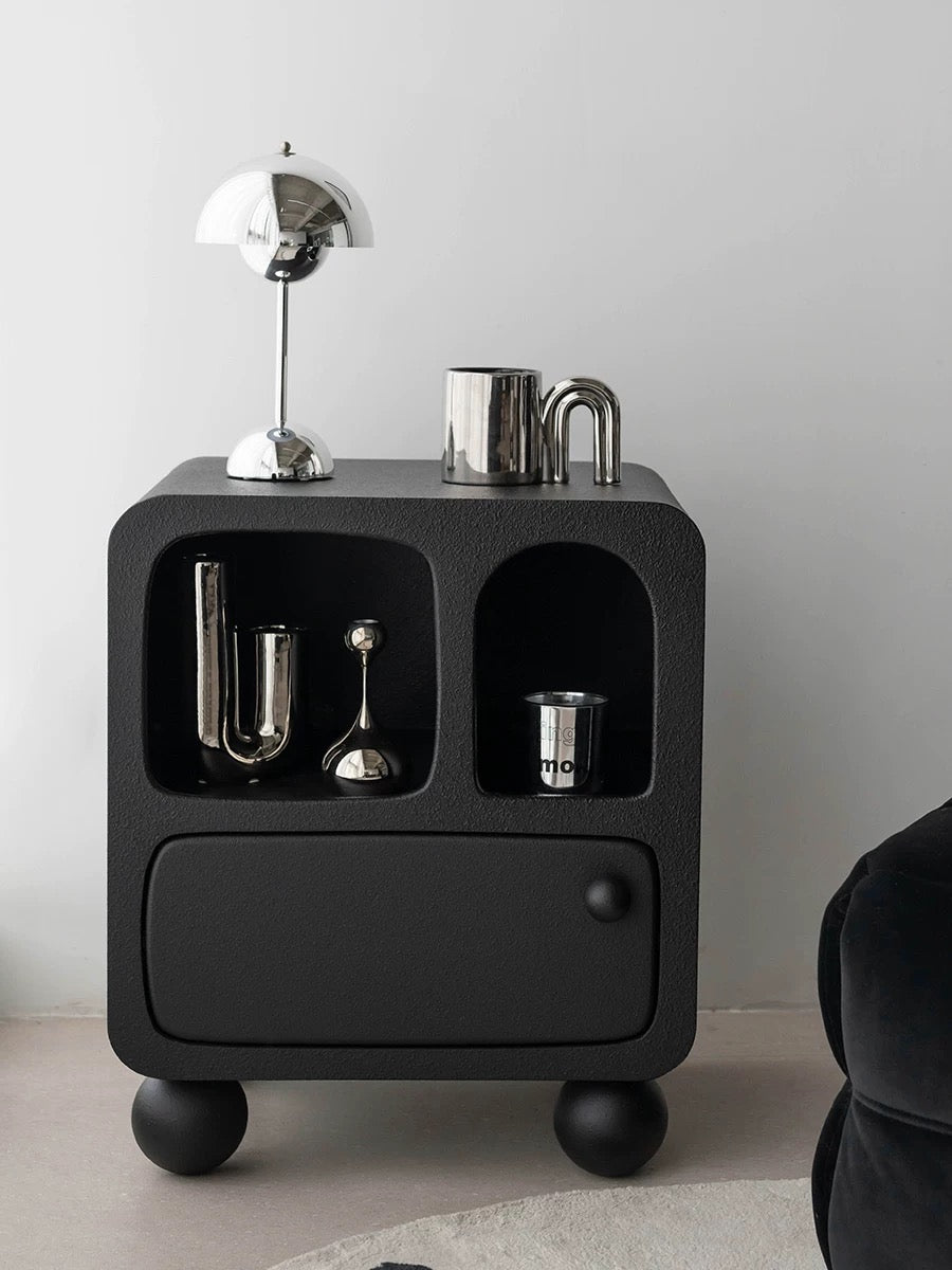 A black nightstand with shelves has a ball knob and round feet, with silver decor in the open compartments.