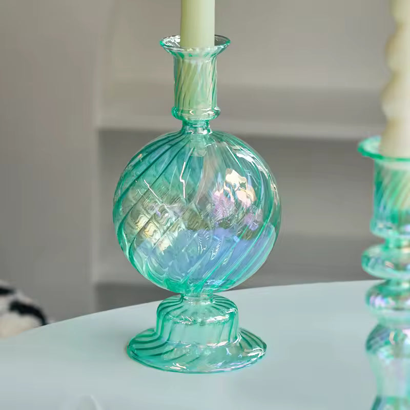Green glass candle holder with a white candle on a light surface.