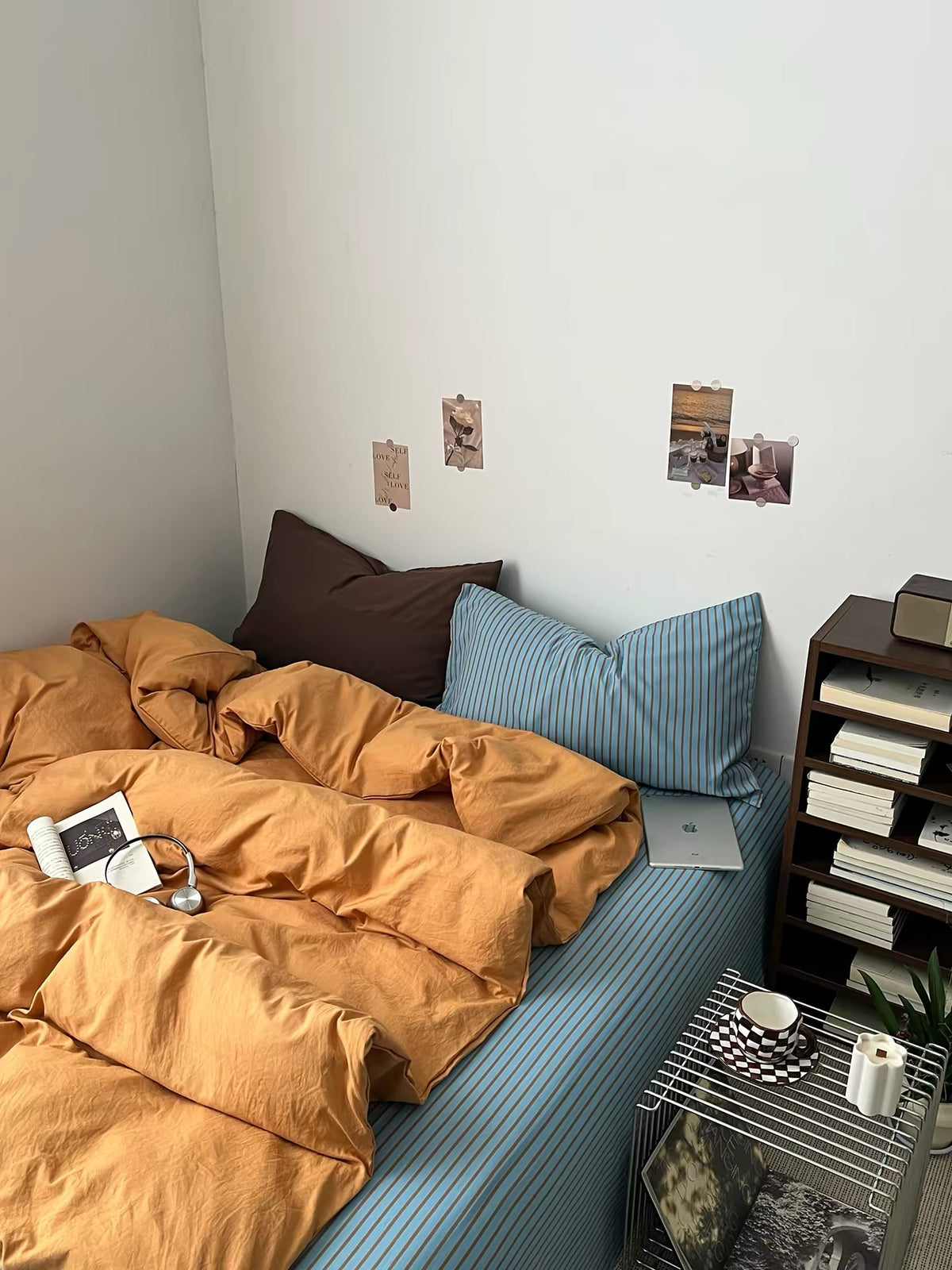 Orange bedding set with a blue striped sheet and brown pillow in a small bedroom