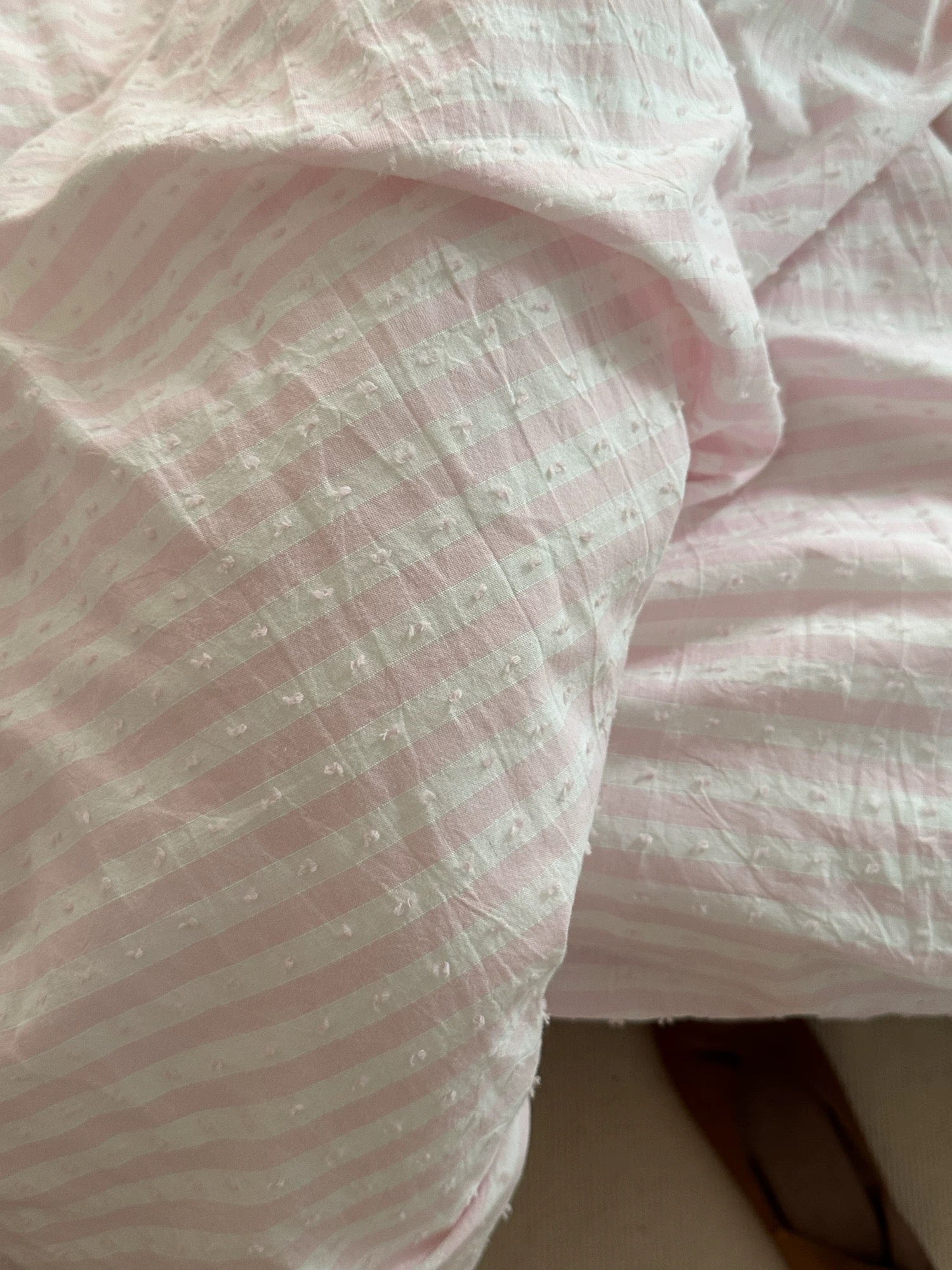 A close-up of light pink and white striped fabric with a textured, slightly crinkled surface.