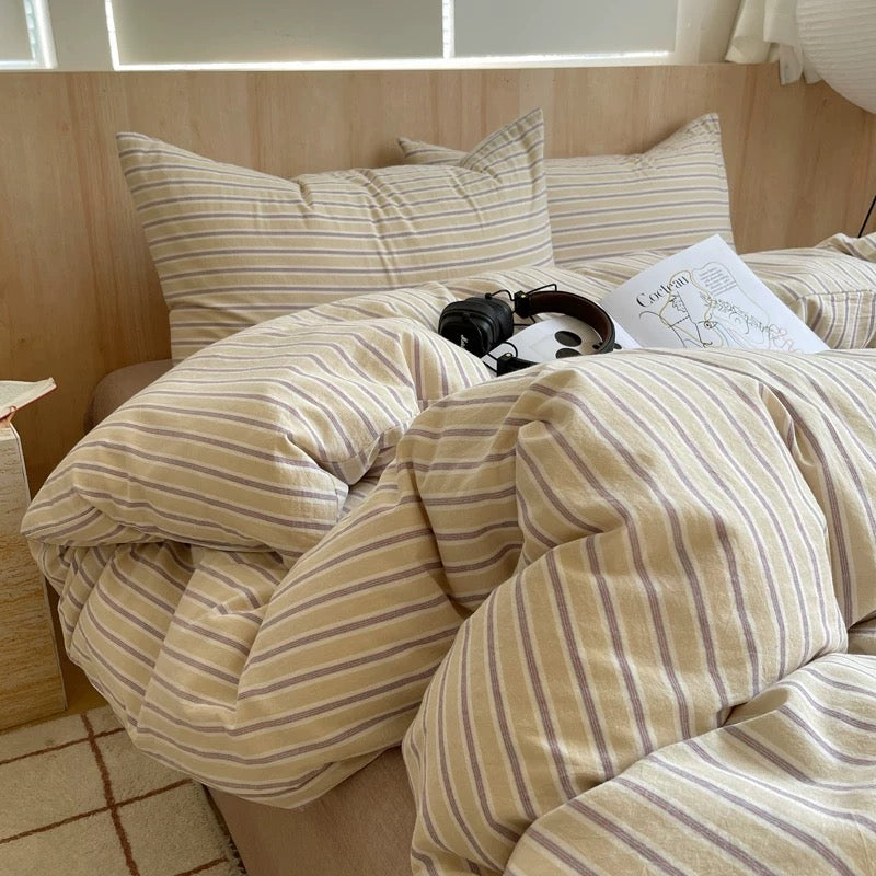 Bed with striped bedding and pillows in a room with wooden walls.