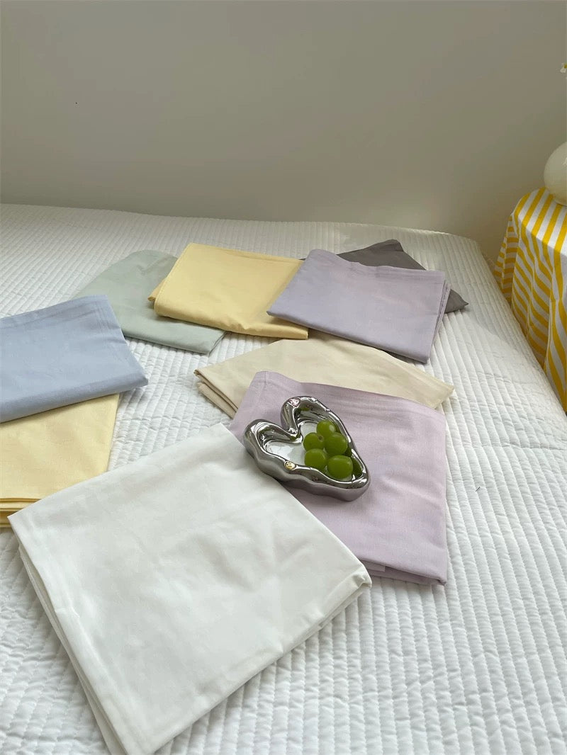Pastel blue, green, yellow and purple sheets are spread across a white bed beside a small silver dish.