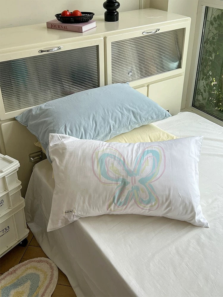 Pastel butterfly pillowcase arranged on a white bed beside pale blue and yellow pillows.