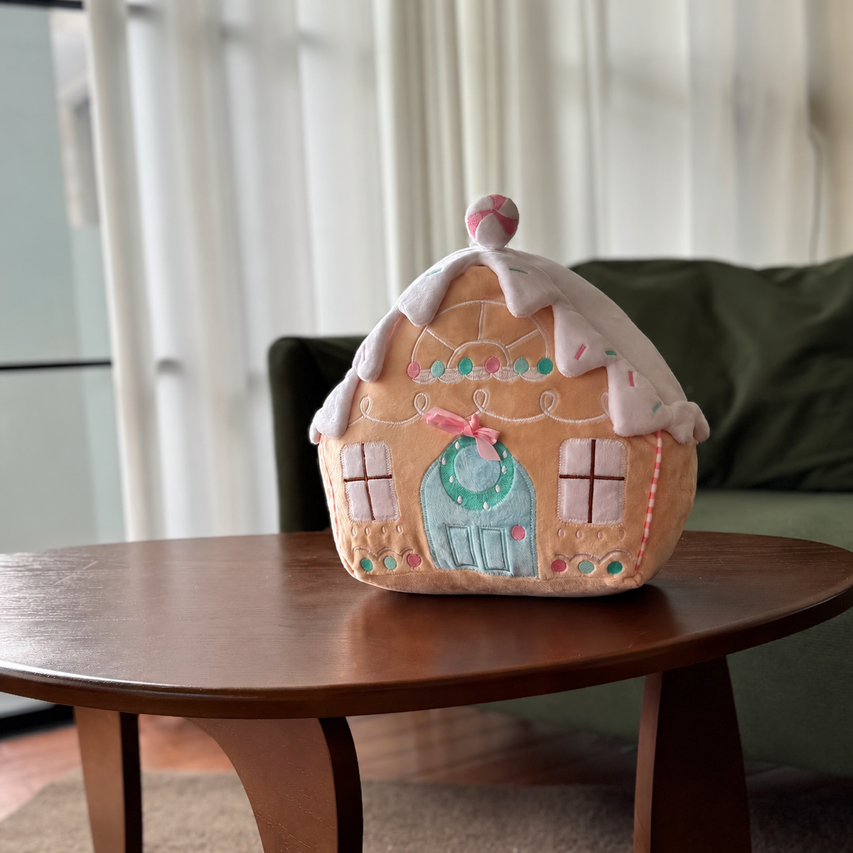 Pastel Christmas cottage pillow with mint green door and snow-covered roof on a wooden table
