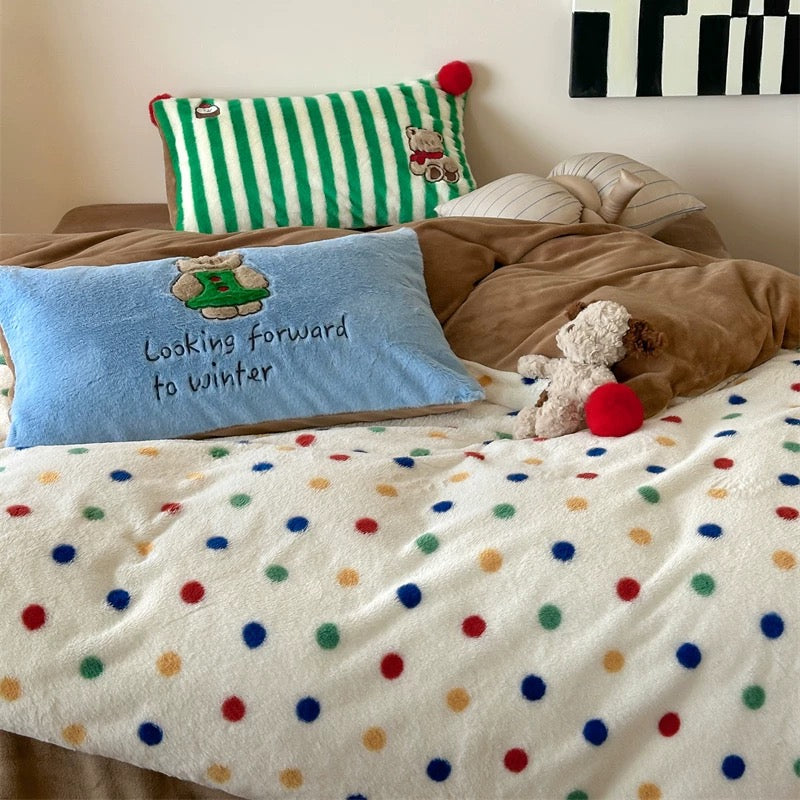 Bed with polka dot blanket, colorful pillows, and teddy bear