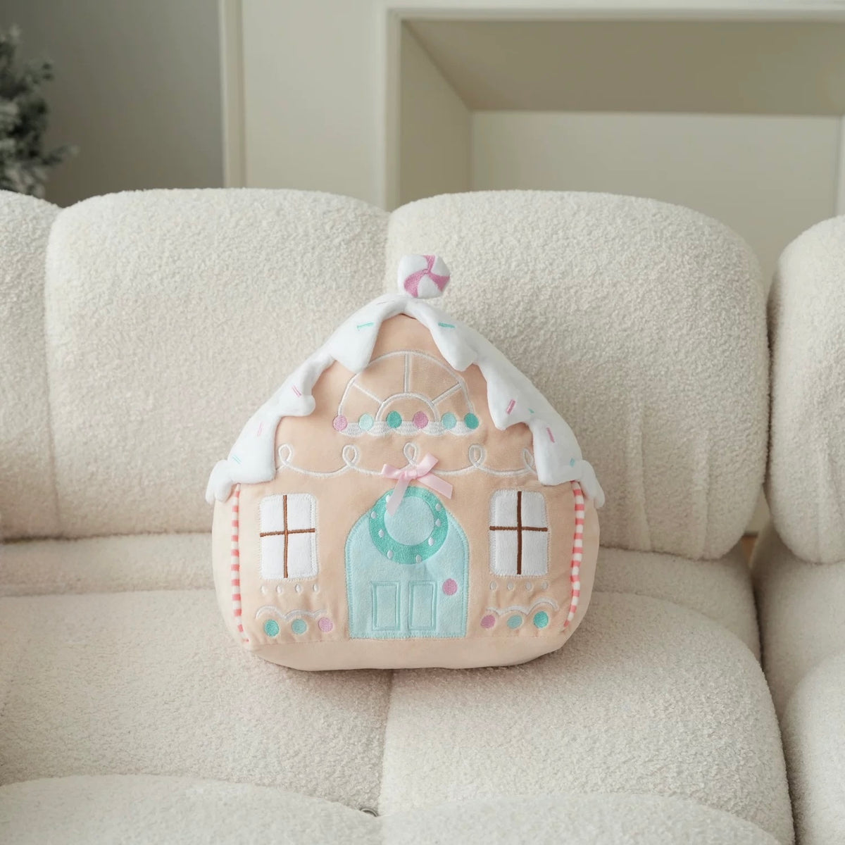 Pastel gingerbread cottage throw pillow with a mint-colored door displayed on a white chair