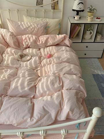 Pink comforter on a bed in a bedroom with a nightstand and decor items.