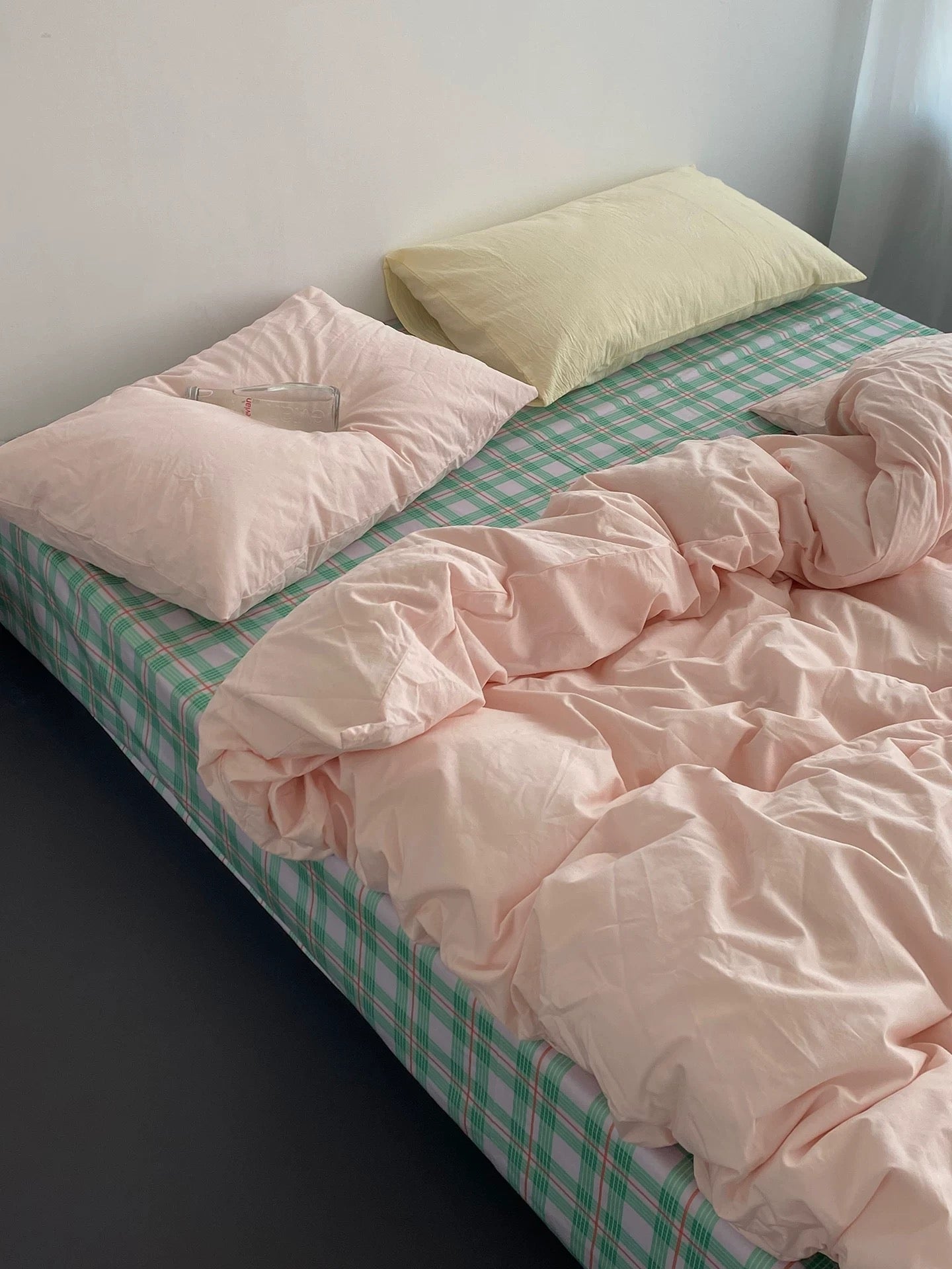 Bed with pink checkered sheets and pillows against a white wall
