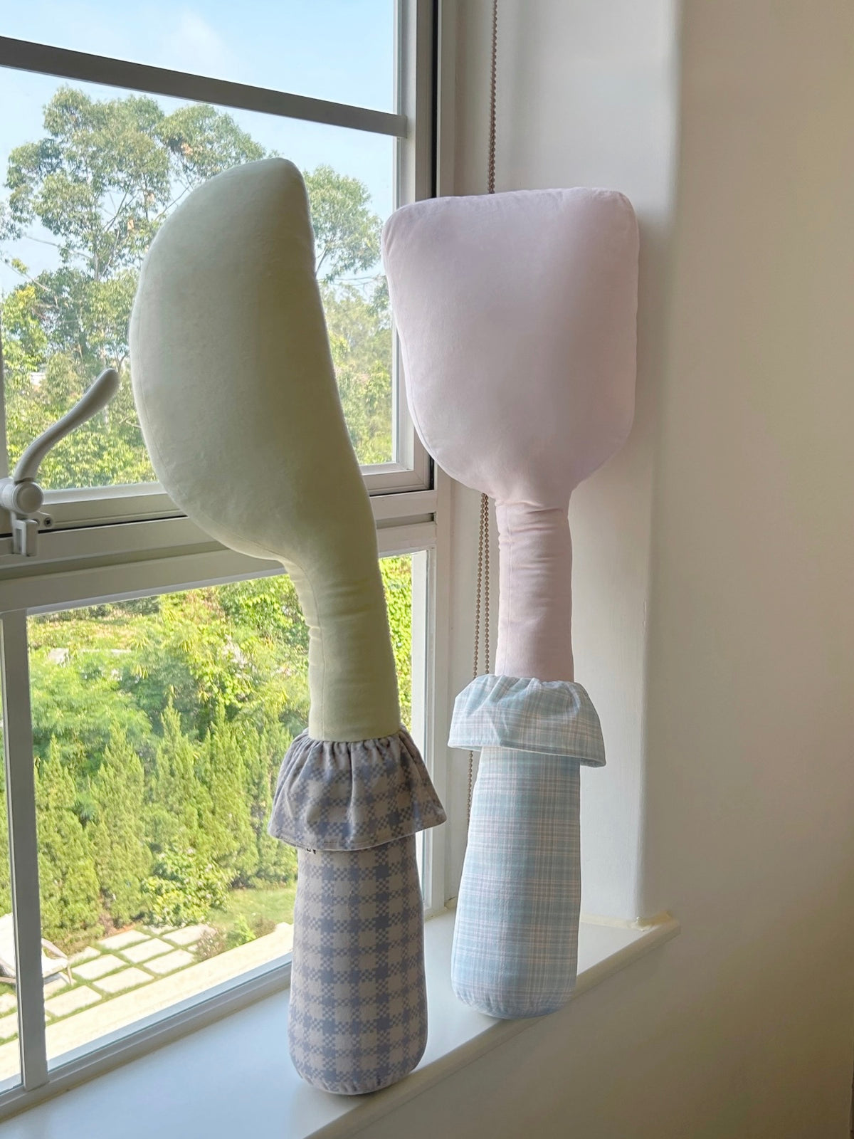 A yellow knife pillow and pink spatula pillow stand together, their pale patterned handles facing forward.
