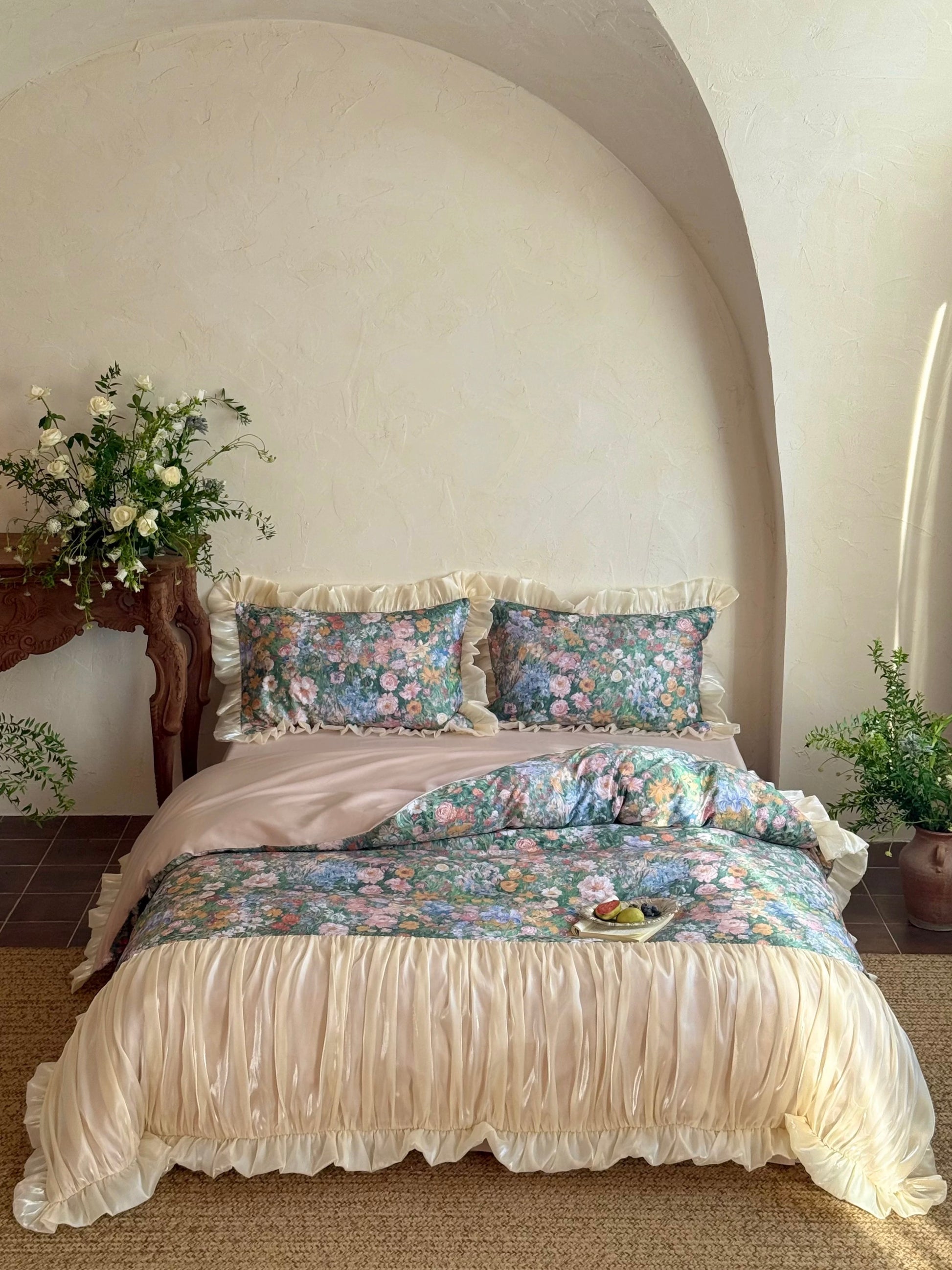 Floral bedding set on a bed in a bedroom with decorative pillows and a vase of flowers.