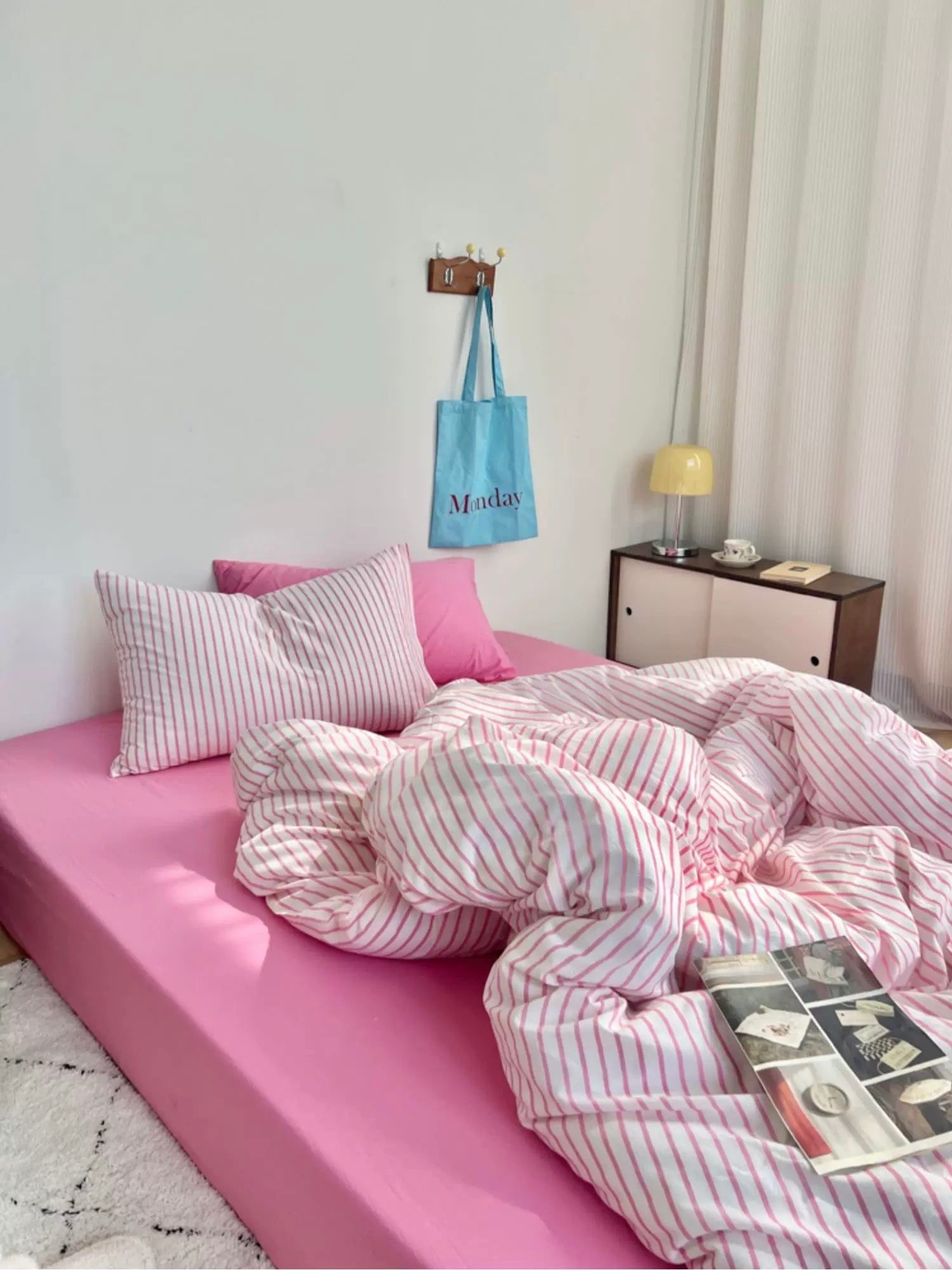 Pink bed with striped bedding in a room with a lamp and wall decor.