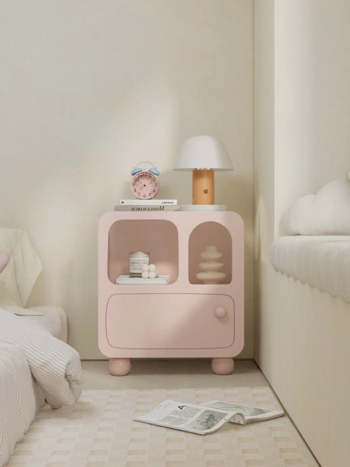 A pink arched nightstand faces forward beside a bed, with round feet below its closed lower drawer.