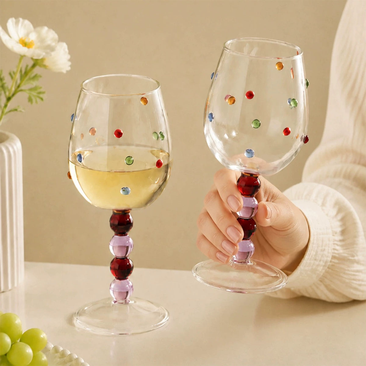 Pink ball stem wine glasses with colorful raised dots, one held by hand