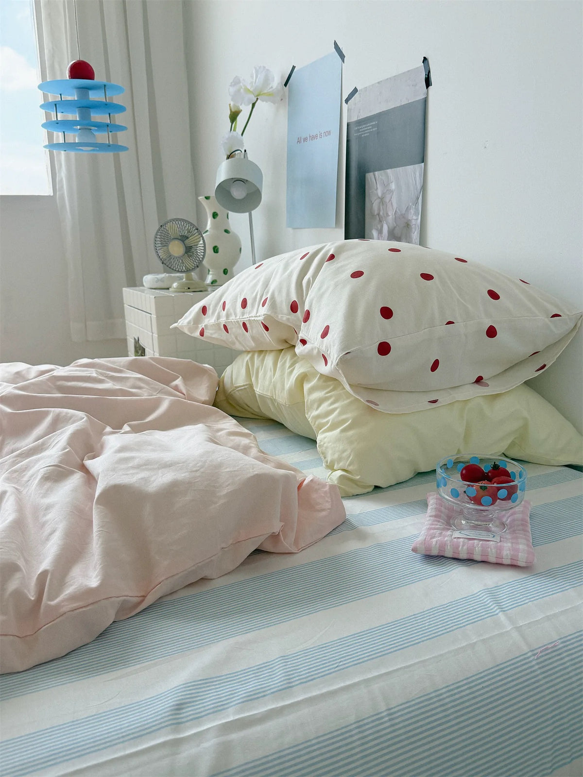 Small red dot and yellow pillowcases beside a window above the pink cover and blue striped sheet.