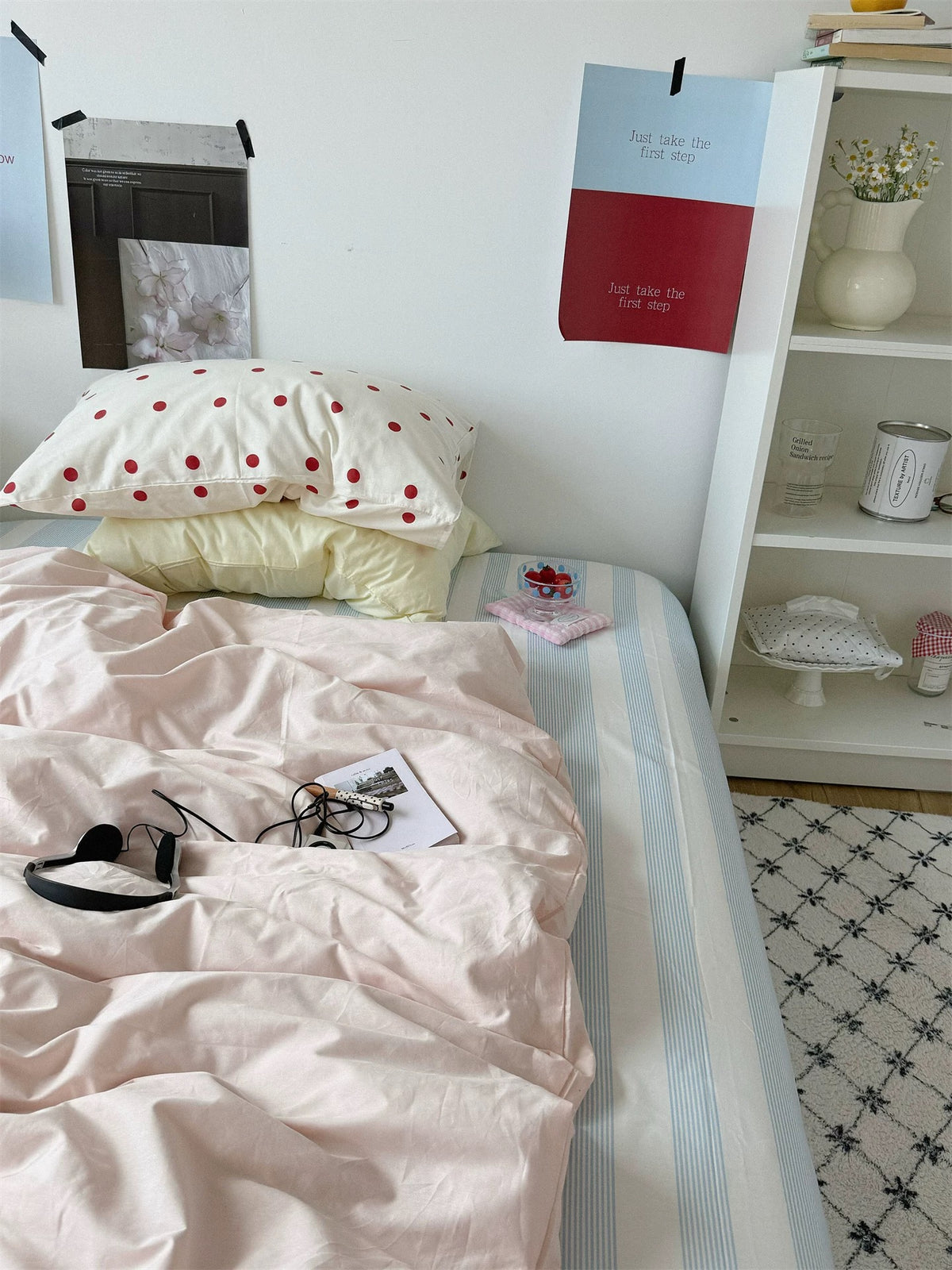 A pink duvet cover lies below yellow and small red dot pillows with headphones on the bed.