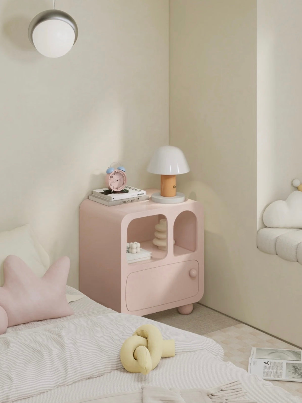A pink bedside cabinet is shown at an angle beside a bed, with a lamp and clock on its rounded top.
