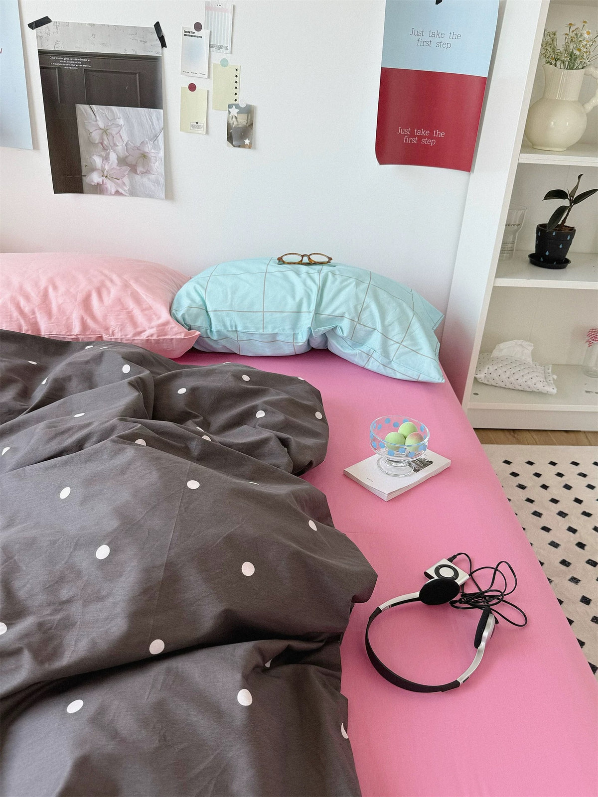 Pink and gray bedding with a baby pink pillow beside a blue checked pillow and small light dots across the cover.