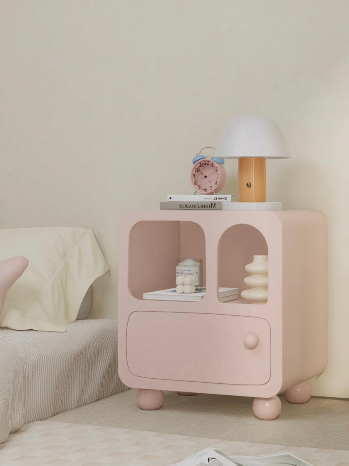 A pink nightstand viewed at an angle has rounded corners and a ball knob beneath two display openings.